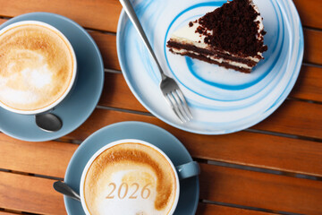 Hello New 2026 Year. Cups of coffee and piece of cake on wooden table, top view