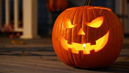 A menacing, traditional jack-o'-lantern with a fiery glow sits on a dark wooden porch, its flickering flame illuminating a classic, spooky Halloween scene.
