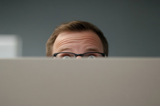 A man looks over a barrier with a startled expression, his eyes wide and filled with surprise. The barrier obscures the rest of his face, creating a sense of anticipation.