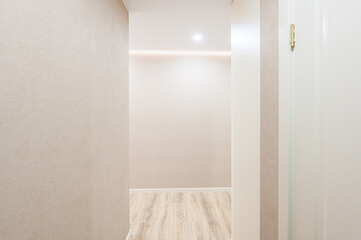 A narrow hallway with textured beige walls, light wood floors, and a white door. A recessed light...