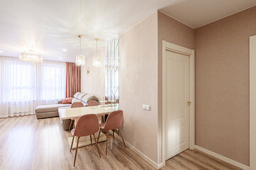 Bright living space with a beige sectional, table with pink chairs, crystal light fixtures, and hardwood floors. Beige and pink walls
