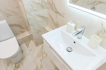 Modern bathroom corner featuring a white sink, chrome faucet, toilet, and marble-patterned tiles...