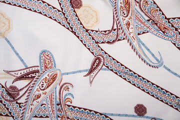 Elegant and luxurious fabric pattern featuring classic brown and blue paisley motifs interwoven with decorative chains and medallions on a bright white background. Ideal for fashion, silk, or vintage 