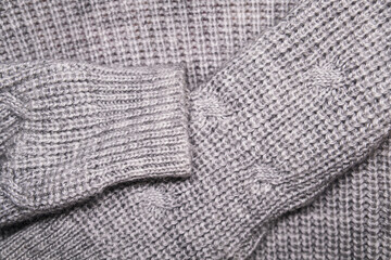 Close-up of a soft gray knitted sweater with visible wool texture and cozy pattern. Warm winter clothing background for fashion, comfort, textile, or handmade knitwear concepts.