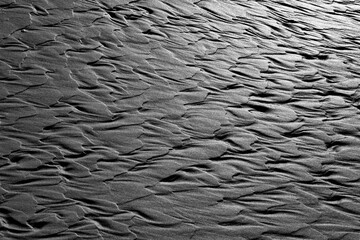 Sand structures with delicate regular shapes on the beach of the North Sea island of Norderney at low tide and low sun. Work of art created by nature in the Wadden Sea NP. Contrasting black and white.