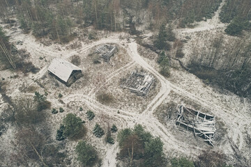 Aerial view of an abandoned village in the forest with destroyed houses against the backdrop of snow and winter landscape