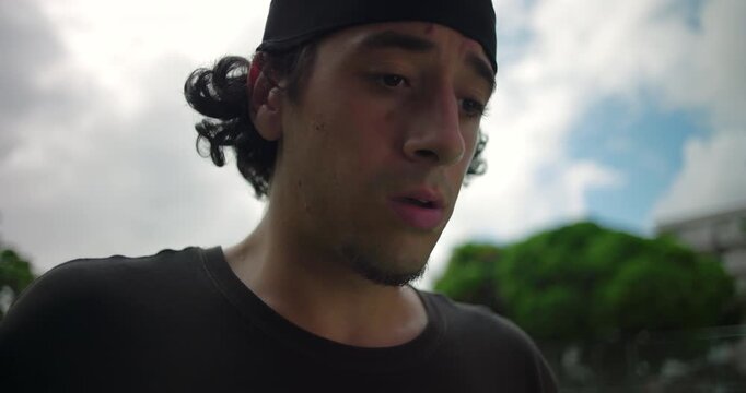Hispanic man outdoors with facial expression of realization and concern, eyes downcast in moment of contemplation, natural light close-up, emotional authenticity and reflection