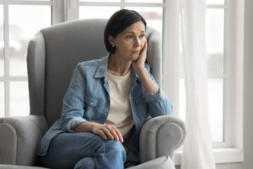 Upset mid aged woman grieve in armchair suffer from menopause