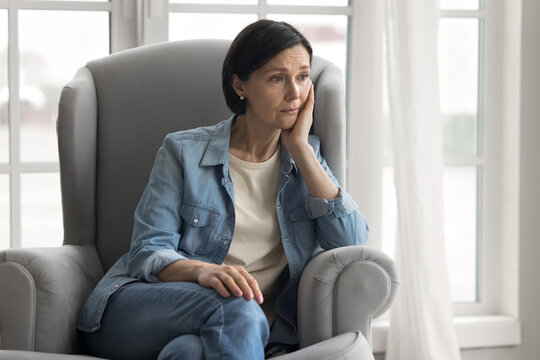 Upset mid aged woman grieve in armchair suffer from menopause