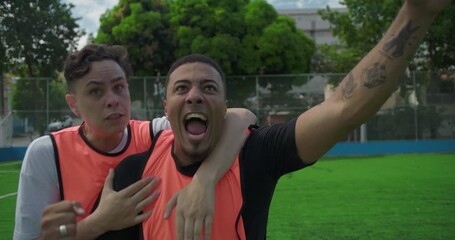 Latin and White teammates celebrate goal on urban soccer field, cheering and raising fists with joy and triumph, showing unity and victory in community sports