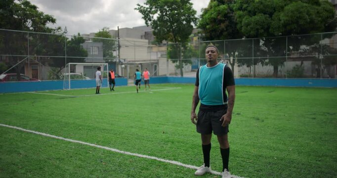 Latin Hispanic man of African descent standing confidently on soccer field during community match, teammates blurred in background, symbol of teamwork, pride, and determination