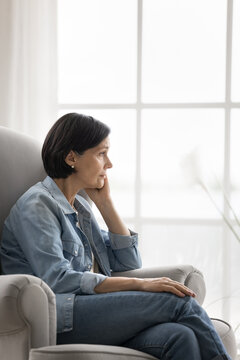 Stressed older woman sitting alone in cozy chair looking aside