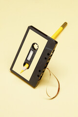 Old Audio cassette tape with a blank label and pencil on the hole. Retro acoustic. Rewind audio cassette tape with tape by yellow pencil on a yellow background. Vintage media concept.