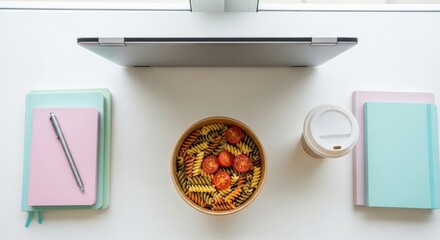 Top view of pasta salad with cherry tomatoes on white desk with notebooks and coffee cup