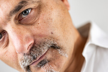 Detailed close-up of a middle-aged man with a tilted head and serious expression, highlighting his blue eyes, mustache, and skin texture.