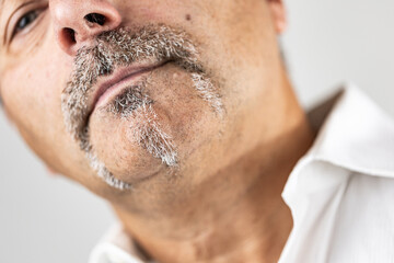 Close-up macro shot of a man’s lower face showing his gray mustache, goatee, and skin texture. The head tilt and tight framing highlight facial detail and masculine features.