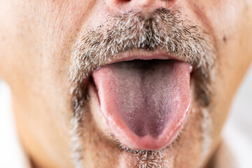 Detailed macro photograph of a man’s face showing his tongue extended below a gray mustache.