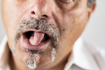 Detailed close-up of a middle-aged man with a salt-and-pepper mustache and goatee extending his tongue toward his nose in a playful gesture.