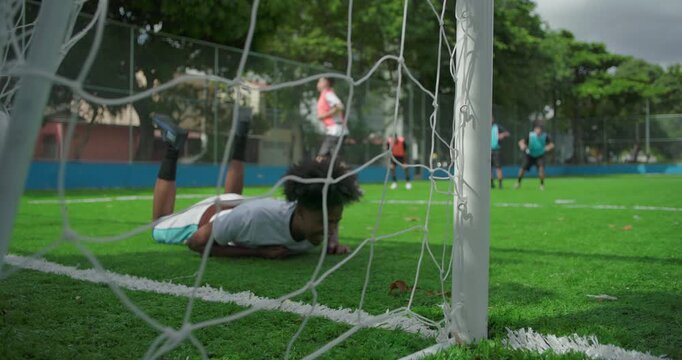 Soccer ball enters goal as African American goalkeeper misses save during casual community match, moment of defeat and teamwork on sunny urban field surrounded by friends - Powered by Adobe