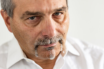 Detailed close-up of a middle-aged man with gray mustache and goatee expressing doubt or skepticism. The intense gaze and furrowed brow highlight emotion and character.