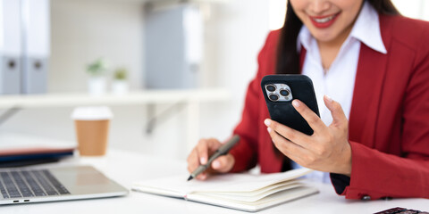 Asian business woman using smartphone and taking notes while working in office.