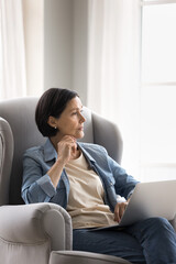 Obraz premium Older woman sitting in armchair with notebook looking at distance