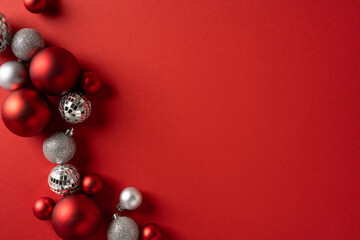 Vibrant holiday scene with red and silver Christmas ornaments arranged along a curved edge, creating a festive focal point on a bold red backdrop