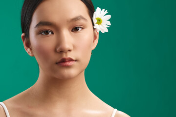 asian woman portrait closeup featuring a calm face with a white flower tucked behind her ear, set...