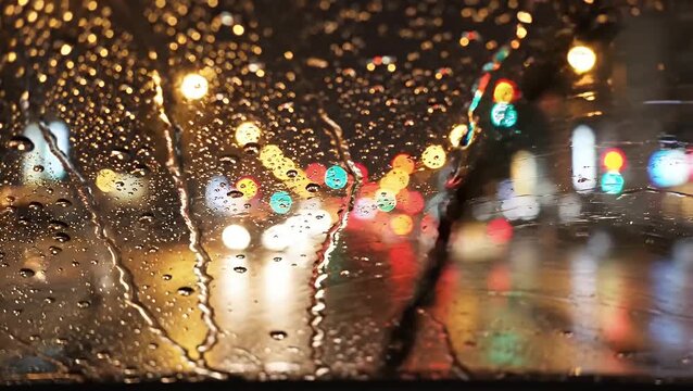 Abstract view of colorful city traffic lights at night seen through a car windshield covered in streaming raindrops