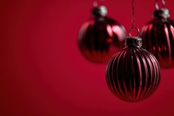 Three deep red metallic ribbed christmas baubles hanging against a solid dark red background with soft focus
