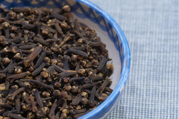 High-resolution macro image of whole dried clove seeds in a blue-patterned ceramic bowl. Aromatic spice commonly used in cooking, baking, and natural remedies. Perfect for culinary and wellness themes
