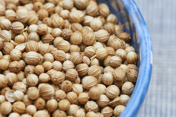 Macro image showing coriander seeds inside a blue ceramic bowl. Widely used as an aromatic spice in cooking and natural remedies. The earthy tone and detailed texture make it ideal for food background