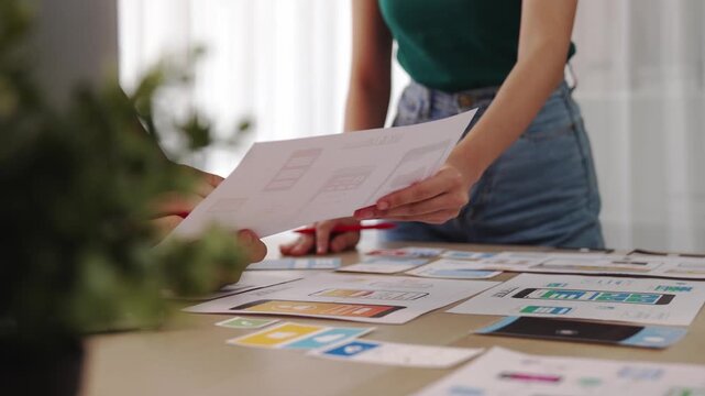 Excellent startup company employee presenting user interface prototype for mobile application to smart co-worker in office workspace. UX UI designer explain function of icon design on paper. Synergic