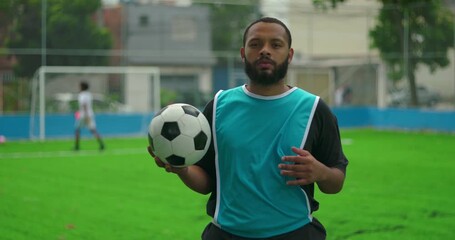 African American man holding soccer ball on green field symbolizing passion, teamwork, and connection to the sport in urban environment, looking confidently at camera - Powered by Adobe