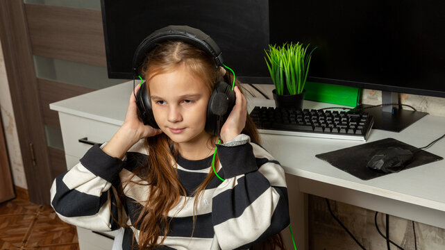 Happy child girl listening music headphones for computer at home.