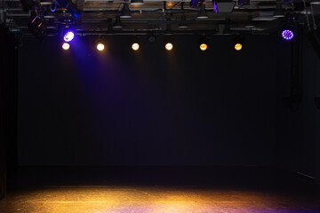 An empty stage with a dark backdrop and warm overhead lights.