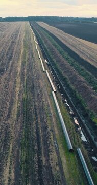 A vertical shot of a pipeline installation in a field, showing the pipes laid out and the surrounding landscape.