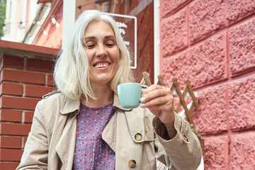 Elderly caucasian female enjoying coffee outdoors in casual attire.