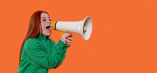 Young woman passionately speaking through a megaphone against a vibrant orange background while wearing a green sweater