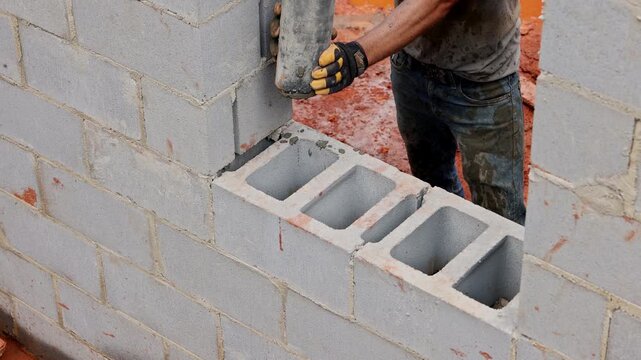 Construction worker is fills wet cement concrete block into wall at building site