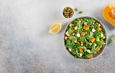 Healthy arugula salad with roasted pumpkin, chickpeas, feta cheese, pistachios on gray background. Top view. Copy space.