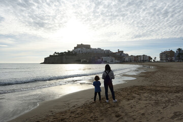 Mother and son watching the sunrise in Peñiscola, Castellon de la Plana, Valencian community, Spain