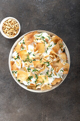 Fatteh with yogurt, crispy pita bread, chickpeas, pine nuts, and herbs in a bowl on a gray background. Lebanese cuisine.