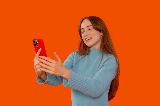 Young woman smiling while using a smartphone in front of an orange background during a casual moment - Powered by Adobe