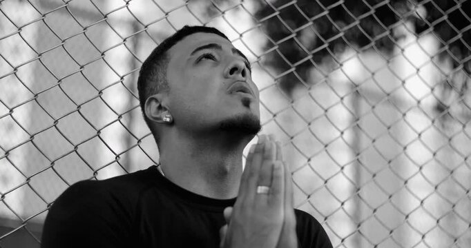 Latin Hispanic man of African descent praying with hands together and eyes lifted upward, expressing faith, hope, and surrender while seeking guidance in monochrome portrait