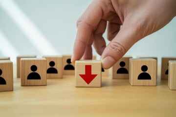Personnel Reduction: A hand strategically selects a wooden block marked with a downward arrow amid a grid of person icons, signifying a crucial decision. 