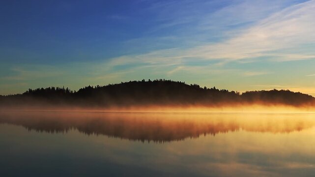 Beautiful autumn sunrise over the sea with golden sunlight, soft fog drifting above the water and forest coastline, peaceful nature scenery in 4K ultra HD