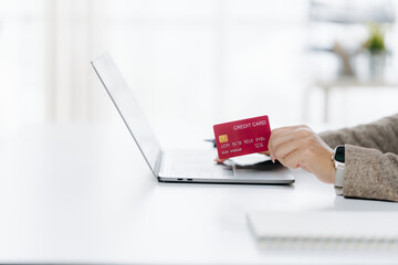 Online transaction: A person securely holds a red card near a laptop, signifying the ease of digital payments.