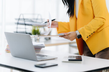 Businesswoman at Workspace: A focused Businesswoman meticulously reviews documents at her desk, with a laptop, mobile, and other stationery scattered around her.
