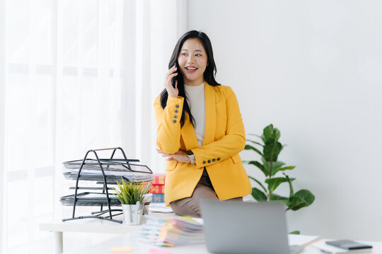 Business Professional on Call: An elegant business professional engages in a phone call within a bright, modern office setting.